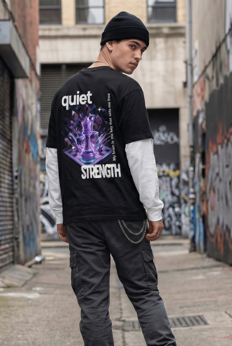 Person walking in an alley with graffiti walls wearing a black 'quiet strength' t-shirt.